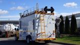 A 2015 Ford Econoline van with a white exterior features a ladder on the back and mounted equipment at the top