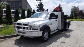 A 2014 RAM 5500 truck with a metallic silver front grille and a flatbed configuration displaying a mounted equipment rack