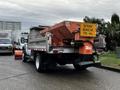 A 2009 Ford F-550 with a large orange salt spreader attached to the back and a "STAY BACK 15 m" sign displayed prominently