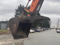 A 2006 Hitachi ZX200LC excavator bucket with a curved edge and teeth is positioned in the foreground, ready for digging or lifting operations