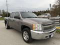 A 2013 Chevrolet Silverado Hybrid in a light gray color with a four-door cab and off-road tires parked on a street