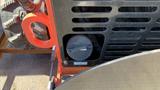 A close-up view of a round cap from the 2024 AGT LRT23 machine partially visible through a grid of ventilation holes with a red handle adjacent to it