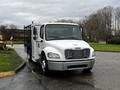 A white 2005 Freightliner M2 106 truck with a flatbed and a black railing along the sides positioned in a parking lot