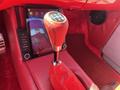 Close-up of a gear shift in a vintage 1962 Ford F-100 featuring a chrome knob and leather boot on a bright red interior