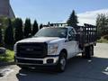 A white 2016 Ford F-350 Super Duty truck with a flatbed and metal side rails parked on a concrete surface