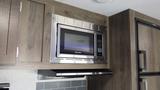 A stainless steel microwave installed in a kitchen cabinet with wood finish in a 2021 Forest River 312BH East To West Della Terra