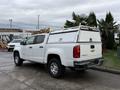 A white 2018 Chevrolet Colorado pickup truck with a utility cap on the truck bed and a ladder rack on top