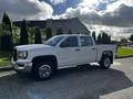 A white 2017 GMC Sierra 1500 truck with a crew cab and chrome accents is parked on a concrete surface showing its profile and side features