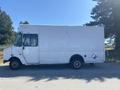 A white 2008 Ford Econoline delivery truck with a boxy shape and side door parked with visible wheels and a blue sticker on the side