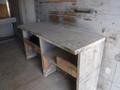 A weathered wooden workbench with two open shelves below and a smooth surface on top