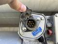 A hand holds open a circular electrical socket with several metal pins visible inside and a label reading Liberty Optic Socket