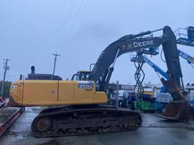 A 2014 John Deere 350G excavator with a yellow body and a black arm and bucket standing on a construction lot with various machinery in the background