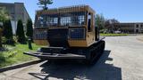 A yellow and black 2015 PowerBully Tracked Flat Deck Equipment Carrier featuring a flat deck and protective grilles on the cab with tracks for off-road mobility