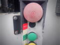 A control panel featuring a large red emergency stop button a black power button and green and yellow operational buttons