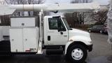 A white 2005 International 4300 bucket truck with an extended hydraulic arm mounted on the cab and a compartment for tools and equipment on the side