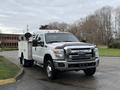 A white 2013 Ford F-350 SD with a utility bed and tools mounted on the side parked on a lot