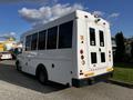 A white 2015 Chevrolet Express bus with large windows and rear doors parked in a lot