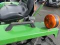 A close-up of a black seat and orange warning light on a green 2003 John Deere 790 tractor with a textured black handle on the side