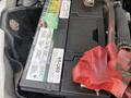 A 2010 Ford F-550 truck battery with a red terminal cover and visible warning labels attached to the battery casing