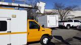 A yellow 2015 Ford Econoline van parked in a lot with a bucket lift attached to the rear