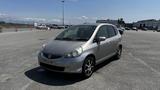 A silver 2006 Honda Fit parked on a paved surface with a slightly dirty exterior and alloy wheels