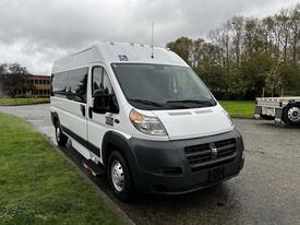 A 2016 RAM Promaster van in white with a high roof and large front windows parked on a wet surface