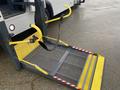 A yellow and gray wheelchair ramp extended from the rear of a 2018 Chevrolet Express with safety markings and a strap for securing wheelchairs