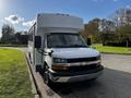 A white 2015 Chevrolet Express bus with a boxy design and large windows parked on the side of a road