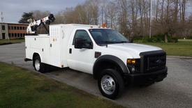 A white 2010 Ford F-550 with a utility bed and a crane mounted on the back positioned at an angle