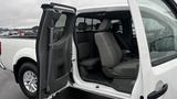 A 2016 Nissan Frontier with an open door showcasing its interior featuring gray seats and modern dashboard elements