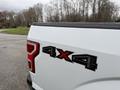 A close-up of the rear badge of a 2018 Ford F-150 showing the 4x4 emblem in red and black on a white truck