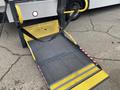 A yellow and gray wheelchair ramp is extended from a vehicle showing textured flooring and safety straps