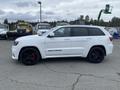 A white 2018 Jeep Grand Cherokee with black wheels and red brake calipers parked on a gravel surface