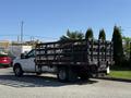 A 2016 Ford F-350 SD with a flatbed and metal side rails parked on a street with a load of plants on the bed