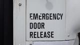 A close-up of a white panel with the words EMERGENCY DOOR RELEASE printed in bold black letters