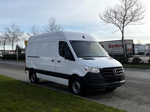 A white 2022 Mercedes-Benz Sprinter van with a black stripe along the bottom and a high roof parked on the side of a road