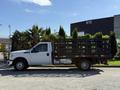 A white 2016 Ford F-350 Super Duty flatbed truck with a black wooden stake bed parked on a gravel surface