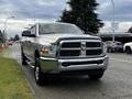 A silver 2012 RAM 3500 pickup truck with a chrome grille and black accents parked on the street with its headlights on