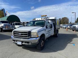 A 2003 Ford F-450 SD truck with a white exterior and yellow markings is parked with a utility bed and light bar on the roof