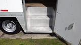 A set of silver diamond-patterned steps leading up into the back of a white delivery truck with a partially open rear door