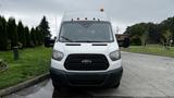 A white 2017 Ford Transit van with an amber beacon light on the roof and a black grille facing forward