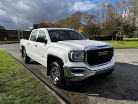 A 2017 GMC Sierra 1500 in white with a chrome grille and shiny wheels parked on a paved area