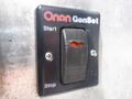 A black control panel with a switch labeled Onan GenSet indicating Start and Stop positions with a visible red indicator inside the switch