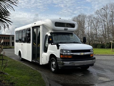 A white 2017 Chevrolet Express bus with a large front windshield and side door open for passenger access