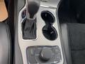 Interior view of a 2018 Jeep Grand Cherokee center console featuring gear shift and cup holders with various control buttons близко к рулю