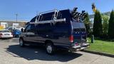 A blue 2013 Ford Econoline van with a raised roof and a ladder rack mounted on top parked beside a grassy area