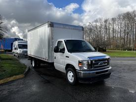 A 2021 Ford Econoline box truck with a white cargo area is parked on a wet road with other vehicles in the background