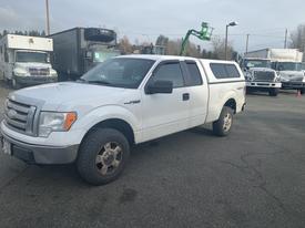 A 2009 Ford F-150 pickup truck with a white exterior and a fitted cap on the bed parked with its front angled to the right