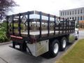 A 2015 International 4400 flatbed truck with a wooden stake bed and safety signage on the sides