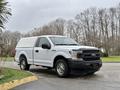 A white 2018 Ford F-150 with a truck bed cover parked on a street showcasing its front profile and wheels